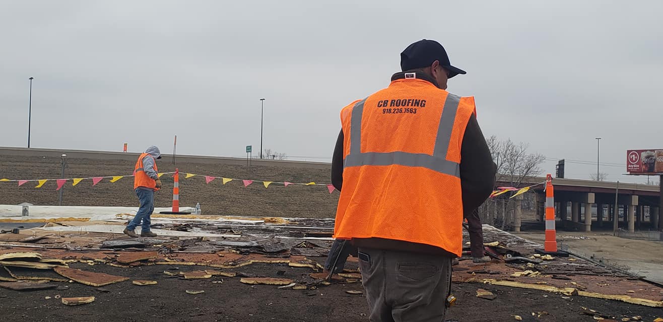 CB Roofing crew member wearing orange safety vest on a commercial roof